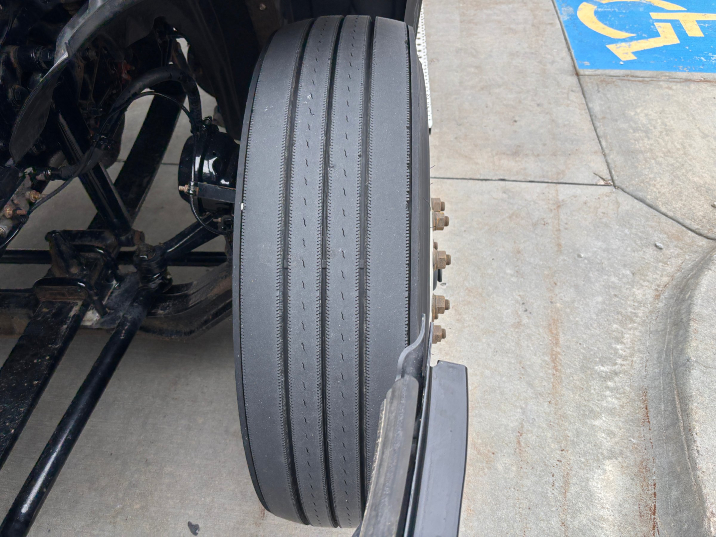Truck wheel and dual-layer tread close-up showing rear of Freightliner daycab chassis with black dual tires and suspension components.
