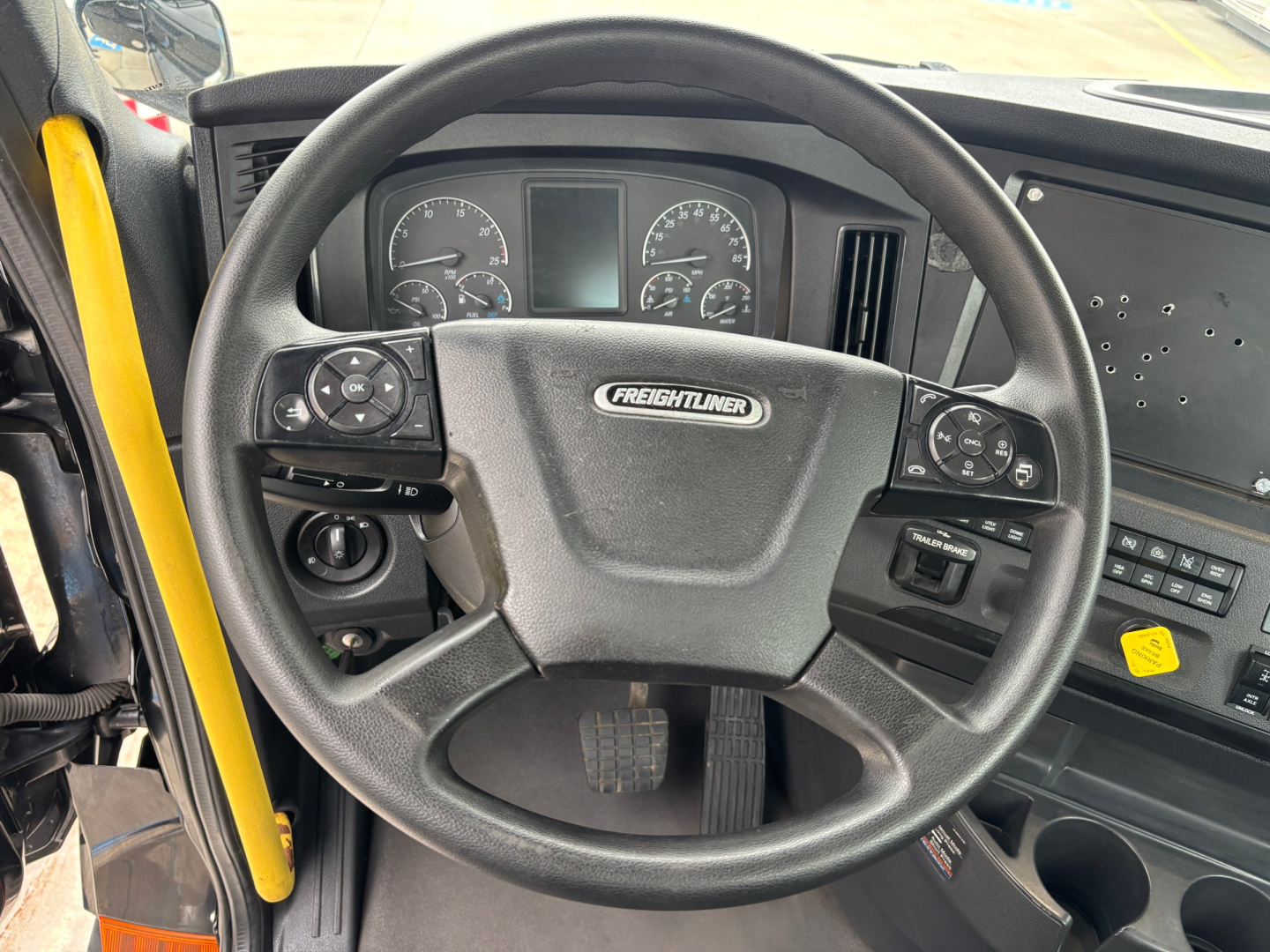Freightliner steering wheel and dashboard inside a conventional daycab truck showing Freightliner badge on the steering wheel and instrument cluster.