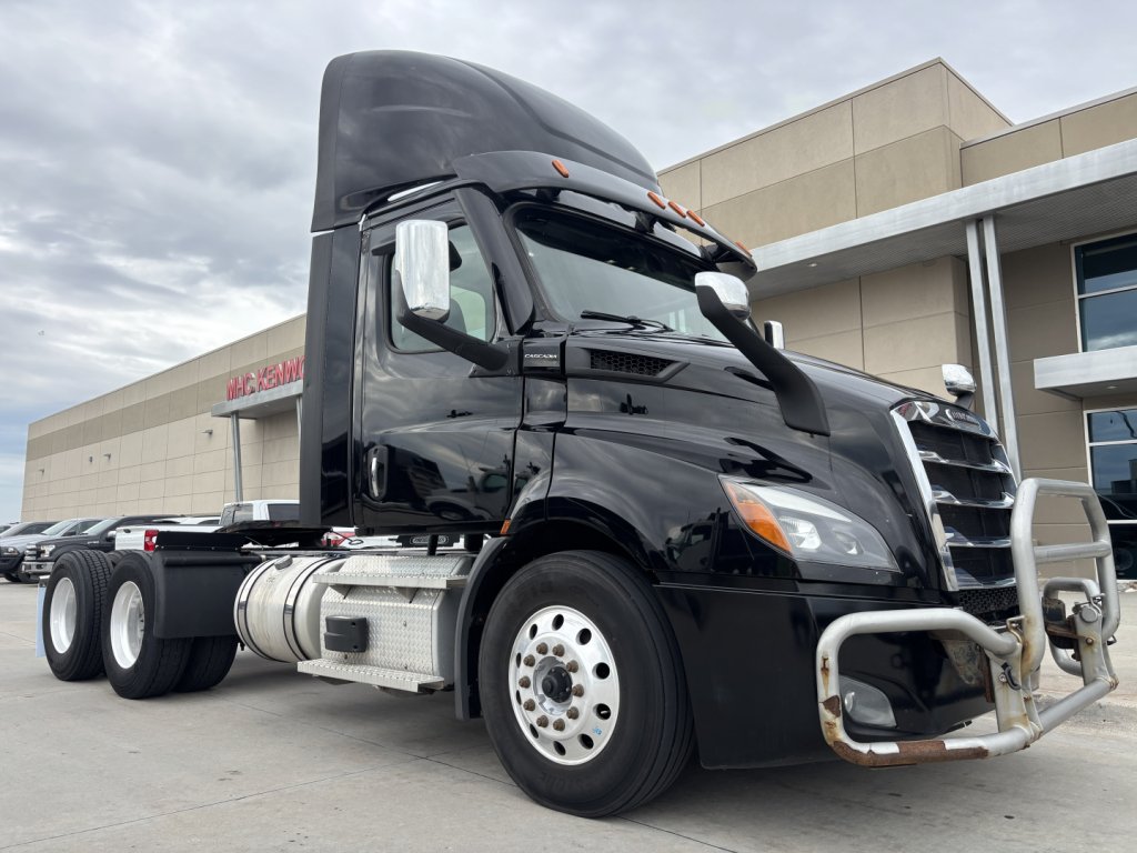 Truck cab showing front grille, bumper guard, and fuel tanks. Visible text includes no specific labels; image shows a black Freightliner daycab tractor from a side angle.