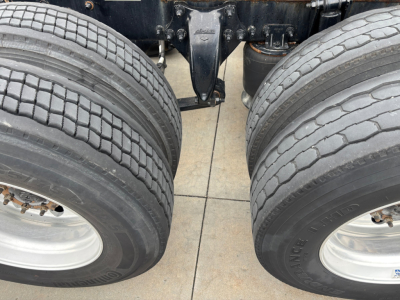 A Freightliner truck chassis view with dual rear wheels and tires, showing suspension and frame components.