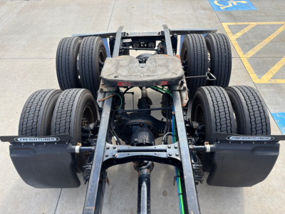 Freightliner PE11664DC chassis rear view showing dual rear axle suspension, drive shaft, and bumper mud flaps with Freightliner branding.