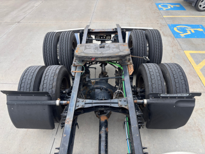 Rear view of a Freightliner truck chassis showing dual rear axles, fifth wheel area, and exposed drivetrain with some rust on frame.