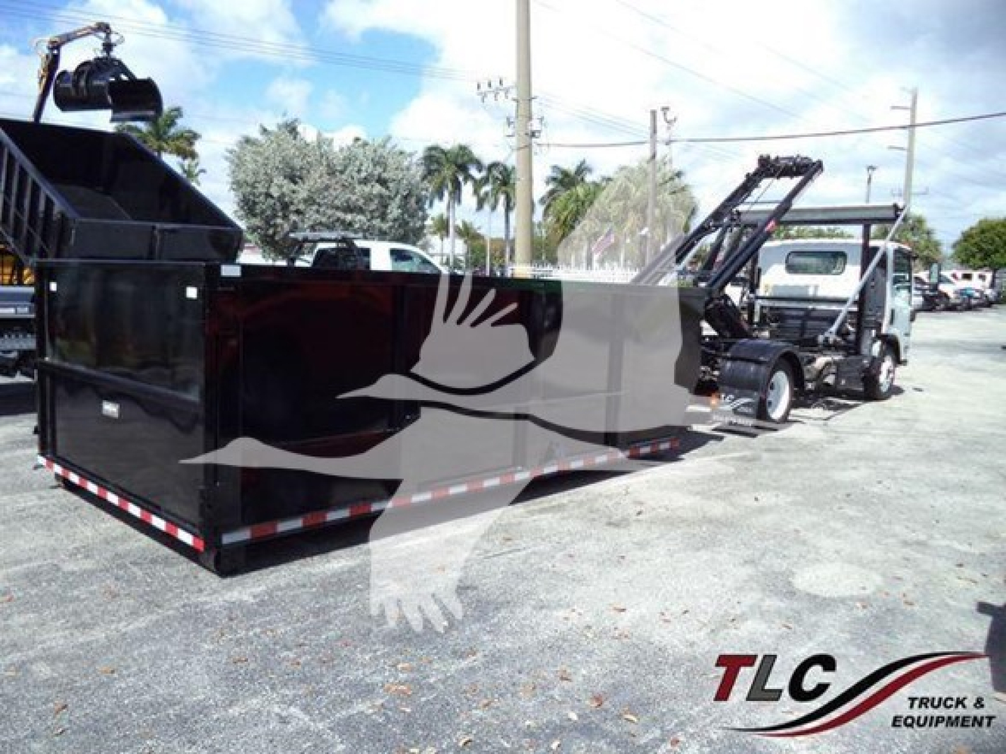 Isuzu NRR truck with a large black roll-off container and a crane/loader in a parking lot.