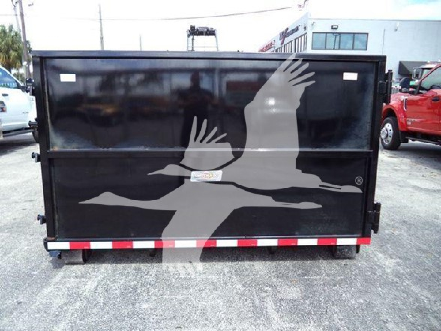Isuzu NRR roll-off dumpster trailer with a large bird graphic on the back doors. Black exterior with red/white reflective striping at the bottom. Small white sticker on the center of the doors.