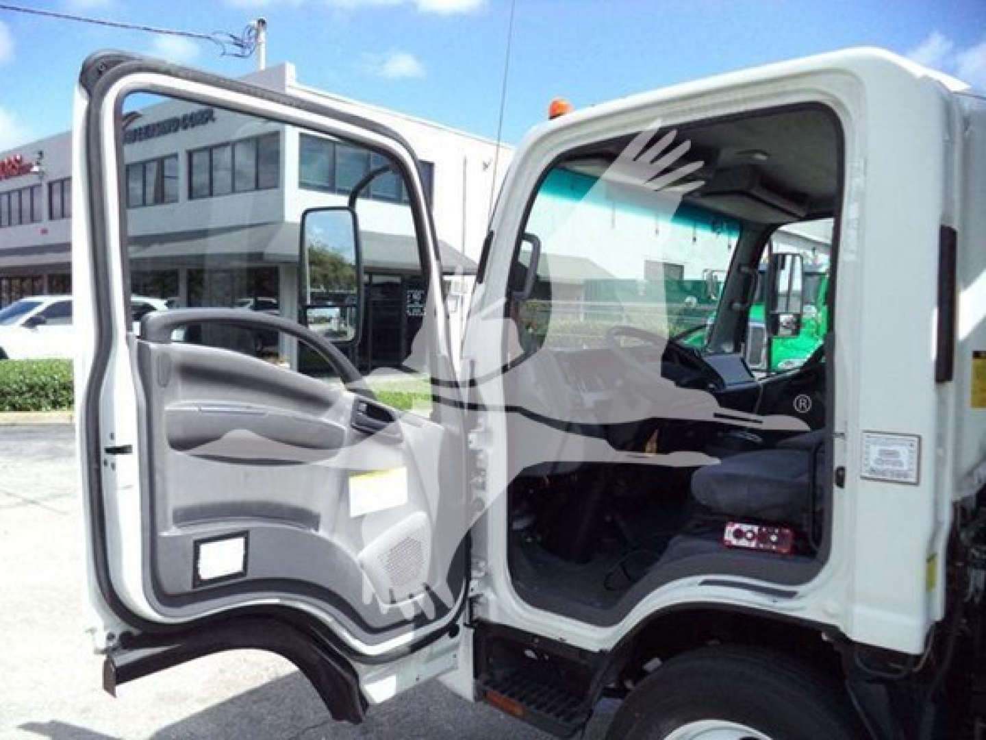 Isuzu NRR truck cab interior with door open showing steering wheel, seat, and dashboard; exterior white cab, rolloff configuration.