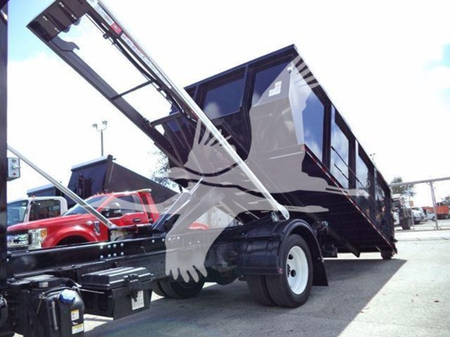 Isuzu NRR dump truck in loading position with hydraulic hoist raised and dumping bed visible.