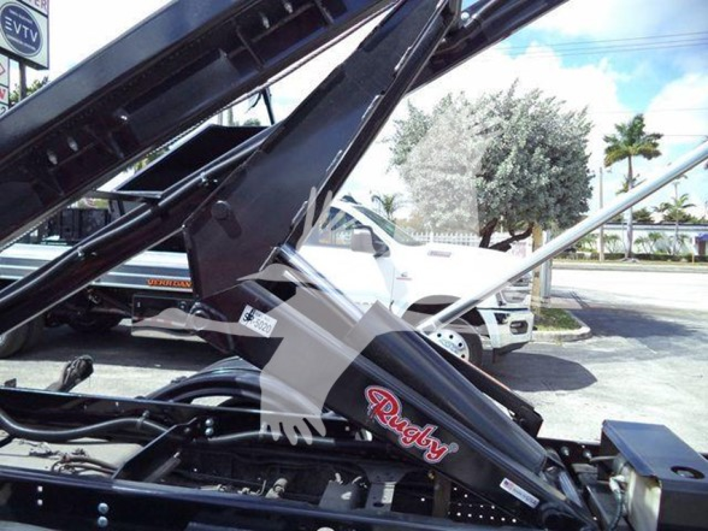 Isuzu NRR truck with roll-off hoist and Reach truck arm showing 'Raugh?' brand decal on black hydraulic arm in a dealership lot