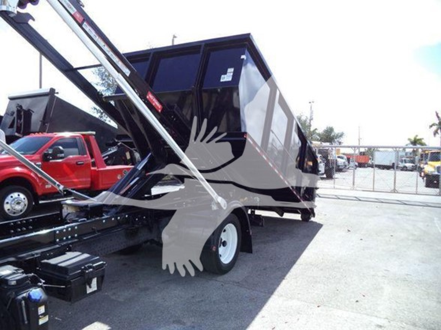 Isuzu NRR roll-off truck with open-top dump bed and crane arm, side view, in a dealership lot