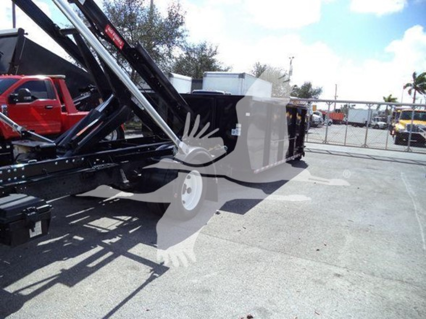 Isuzu NRR roll-off truck side view showing hydraulic lifting mechanism and cargo bed with white wheels.