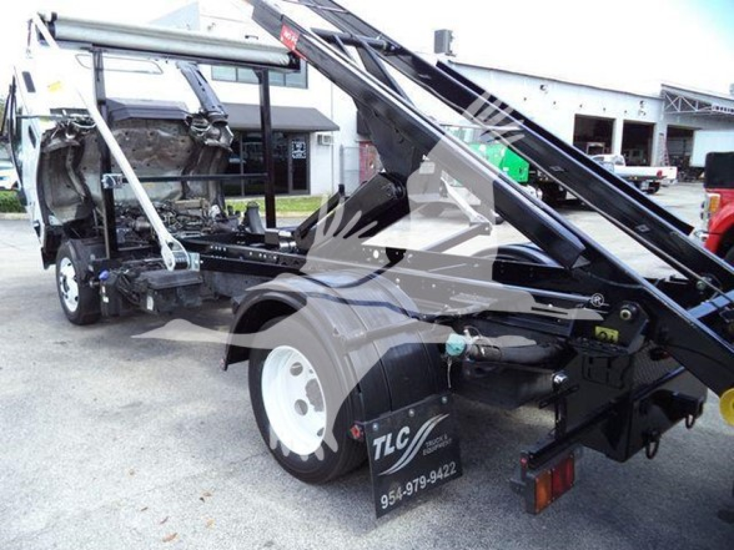 Isuzu NRR roll-off truck rear view showing hydraulic hoist and chassis with TLC logo and contact number; mid-section of cab removed, VIN and stock details not visible in text.