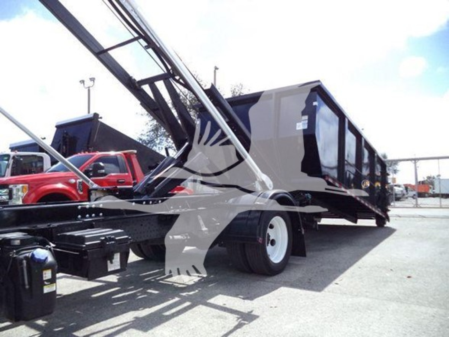 Isuzu NRR roll-off truck with crane arm extended, black long body, white wheels, and empty dump container on a dealership lot.