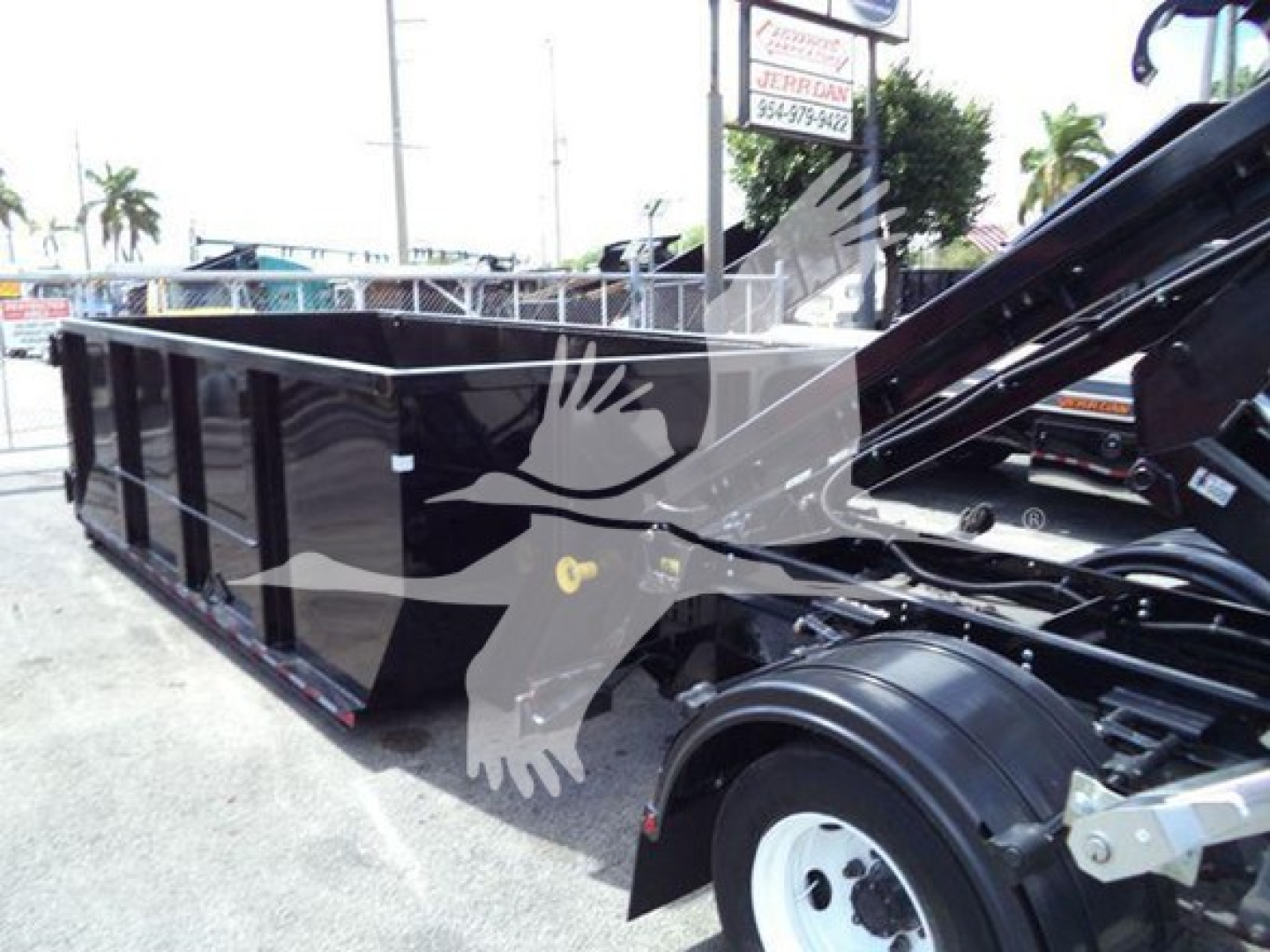 Isuzu NRR roll-off truck chassis with long black dump body and hydraulic hitch, side view