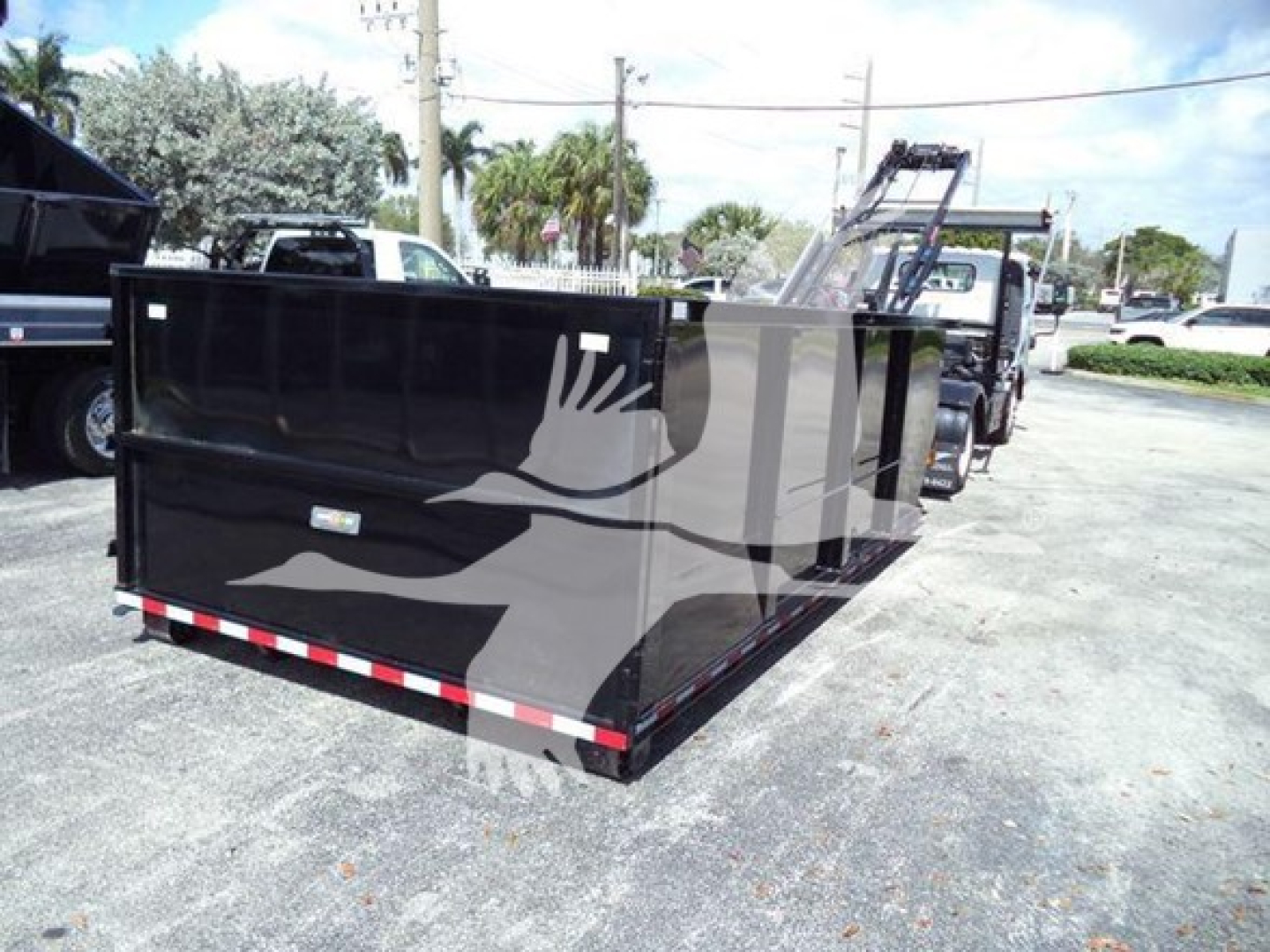 Isuzu NRR roll-off truck in yard with a large black dump box showing a side graphic.