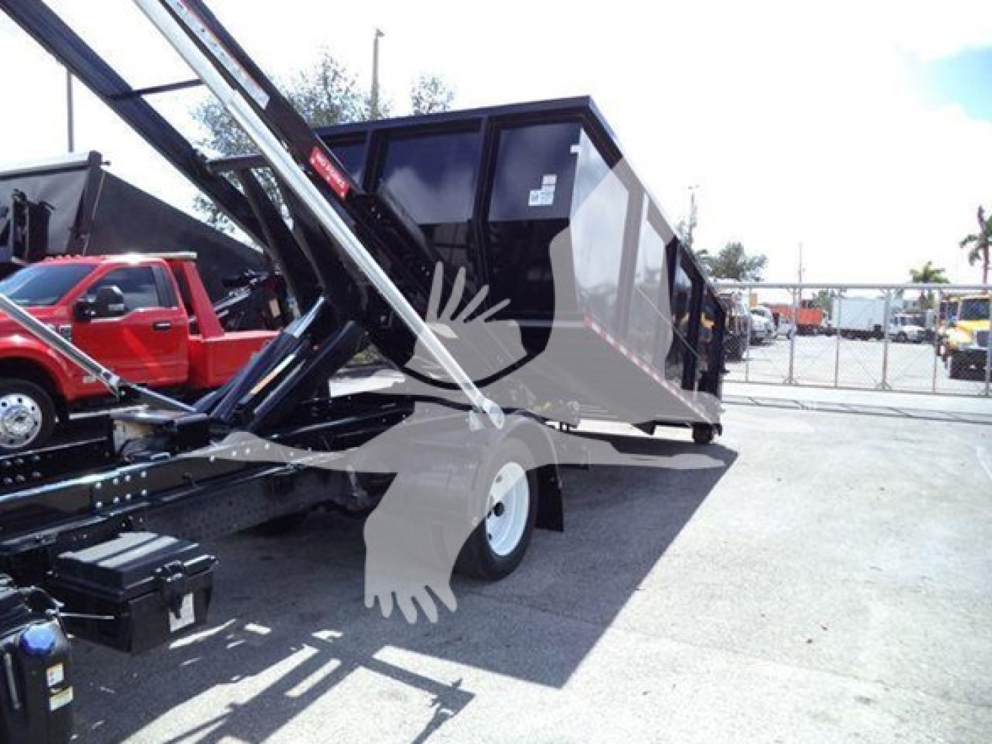 Truck scene showing a Isuzu NRR roll-off truck with hydraulic lifting arms and a dumping container in a yard.