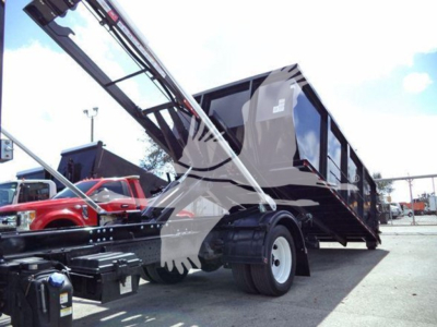 Isuzu NRR roll-off truck with hydraulic crane/dump bed visible; front side shows wheel, container, and metal framework.