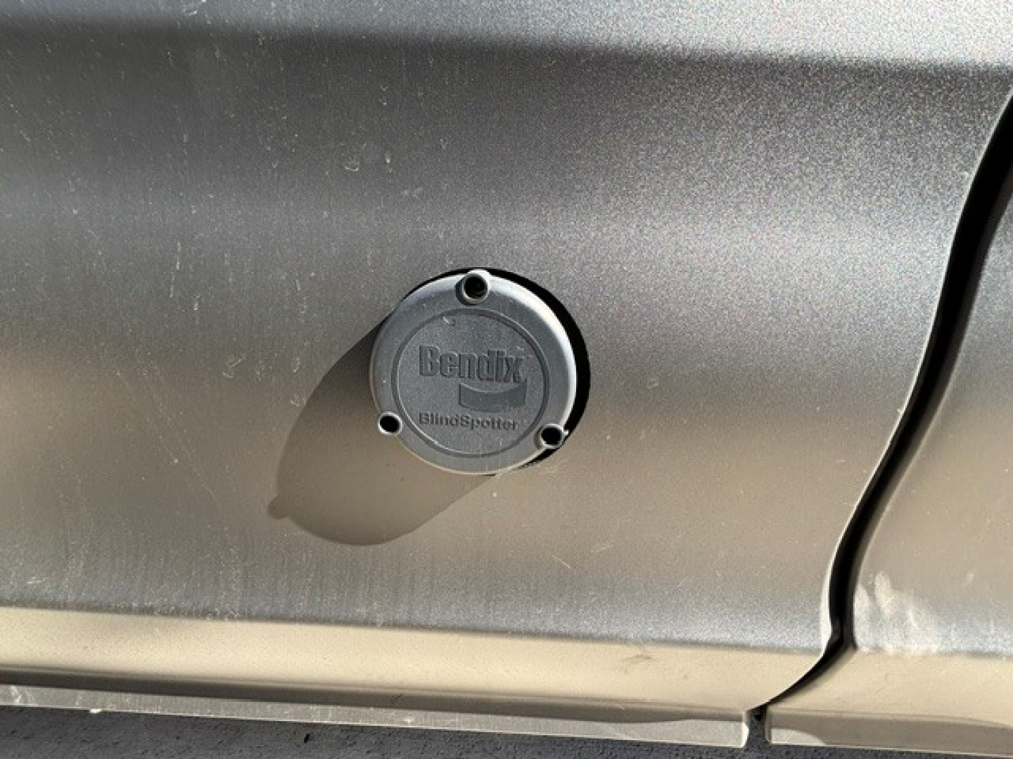 Bendix BlindtSpotter cover on a Peterbilt 579 door panel with circular cap and embossed text, metal body panel with light reflection.