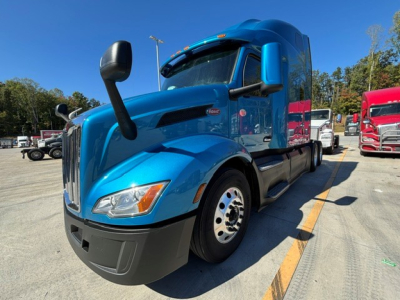Peterbilt 579 conventional sleeper truck in blue, front three-quarter view with side mirror, showing VIN and stock available text not visible.