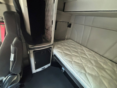 Interior view of a 2022 Peterbilt 579 sleeper cab with a quilted mattress, side cabinetry, and a front passenger seat visible.