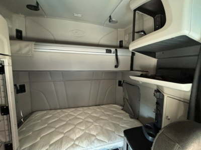 Peterbilt sleeper cab interior showing bunk area with quilted mattress, overhead storage, and side cabinets.