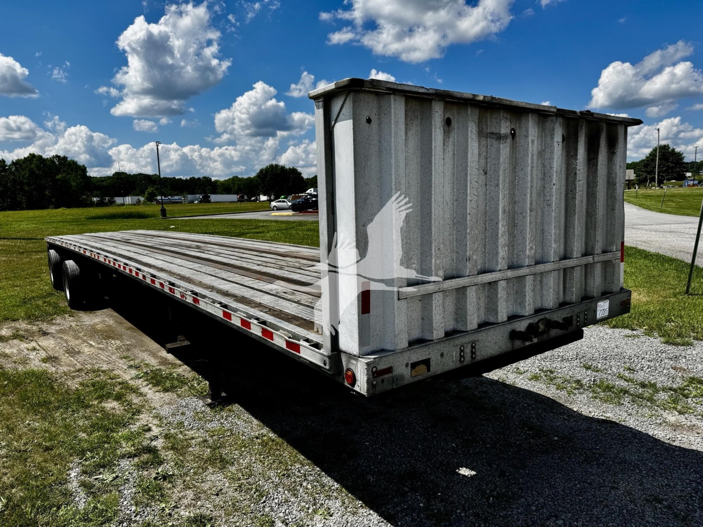 Flatbed trailer showing a long dual-axle frame with a tall dump-style rear end and weathered gray metal surface.