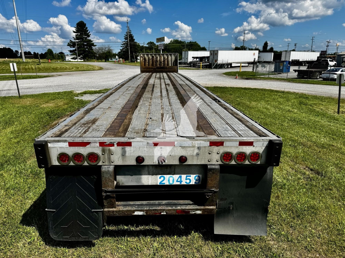 Flatbed trailer rear view showing license plate 20456, taillights, mud flaps, and weathered wooden deck.