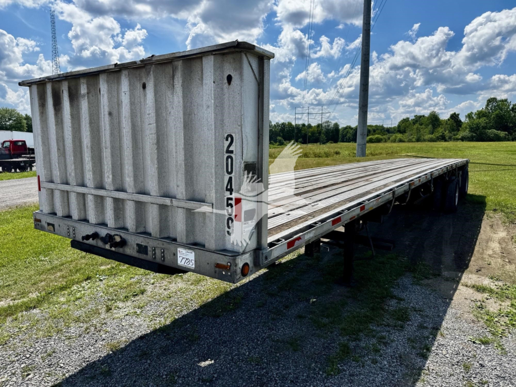 Flatbed trailer showing a gray Transcraft Eagle II with tall cage at front, long wooden deck, rear lights, and support legs; markings 2045 on vertical bar and 2045? visible; VIN/stock not on trailer surface; clear blue sky.