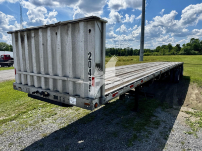 Flatbed trailer showing a gray Transcraft Eagle II with tall cage at front, long wooden deck, rear lights, and support legs; markings 2045 on vertical bar and 2045? visible; VIN/stock not on trailer surface; clear blue sky.