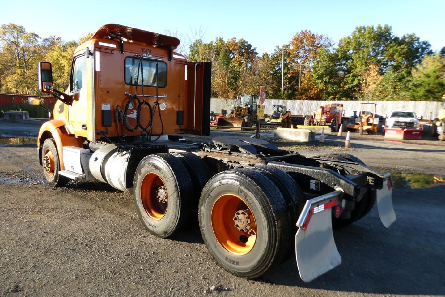 Side view of a used orange 2021 Peterbilt 579 conventional daycab truck chassis with dual rear axles and wheel mud flaps.