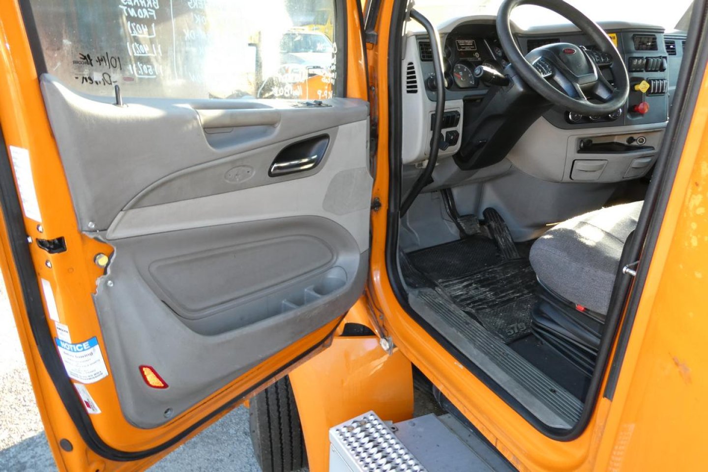 Peterbilt 579 cab interior and open door showing steering wheel, dashboard, and entry steps in orange truck.