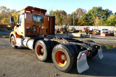 Side view of a used orange 2021 Peterbilt 579 conventional daycab truck chassis with dual rear axles and wheel mud flaps.