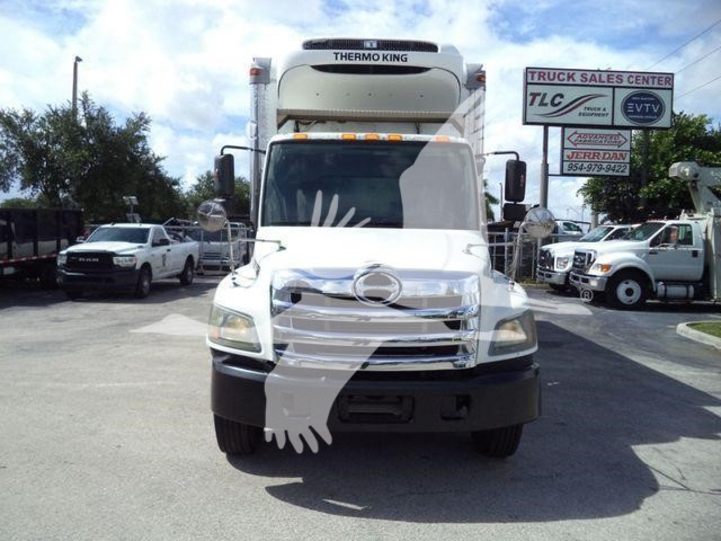 Front of a white refrigerated Hino truck with Thermo King unit on top; vehicles and a sign in the background.