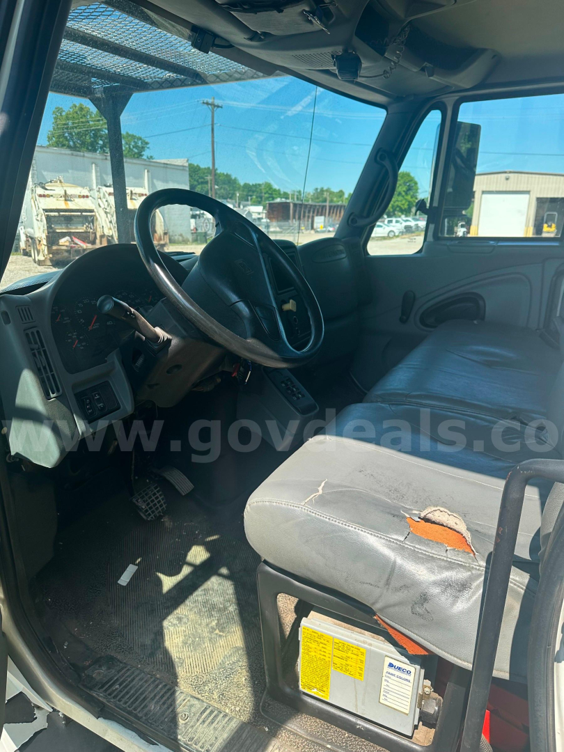 Interior of a 2006 International 4300 truck cab showing steering wheel, dashboard, and worn driver seat with torn upholstery; visible tags under seat and dashboard controls.