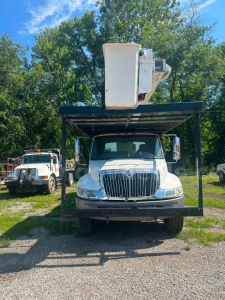 Truck front view of a 2006 International 4300 bucket truck with boom raised in white bucket, grille with International emblem, on a rack over the cab.