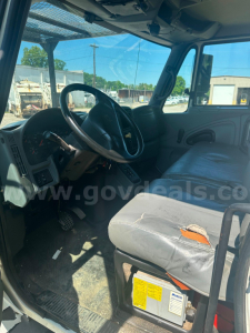 Interior of a 2006 International 4300 truck cab showing steering wheel, dashboard, and worn driver seat with torn upholstery; visible tags under seat and dashboard controls.