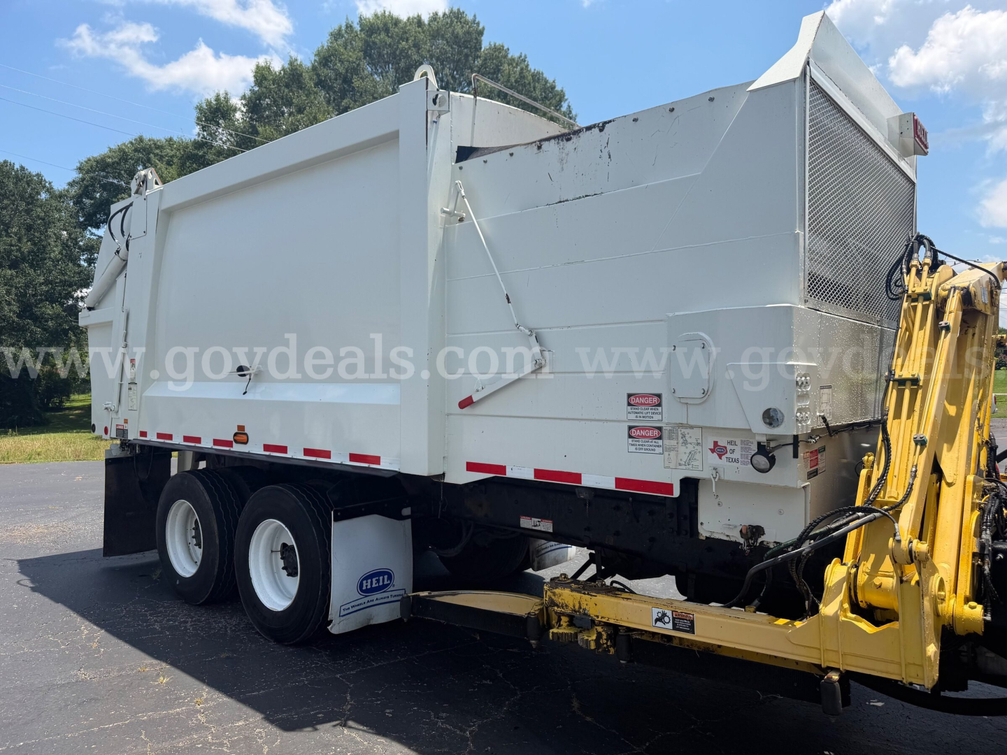 Mack LR dump truck body with front-mounted hydraulic system and white cargo bed, rear wheels visible, stock number plate and warning decals on side.