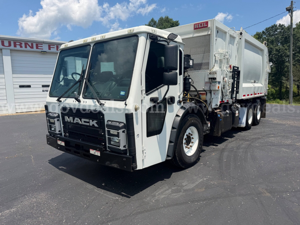 Mack LR garbage truck front-left angle showing cab and dump body with Mack grille and hydraulic lines.