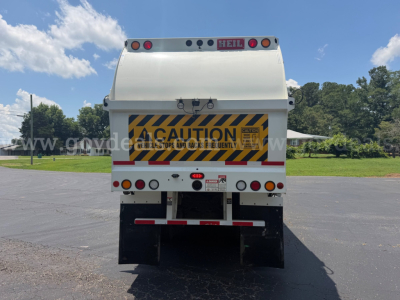 Rear view of a white Mack LR dump truck with yellow and black caution sign on tailgate, multiple lights, and taillight assembly.