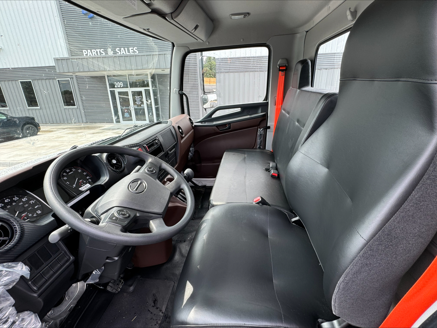 Truck cab interior showing steering wheel, dashboard, and bench seat with black leather upholstery in a 2025 Hino L7 cab-forward truck.
