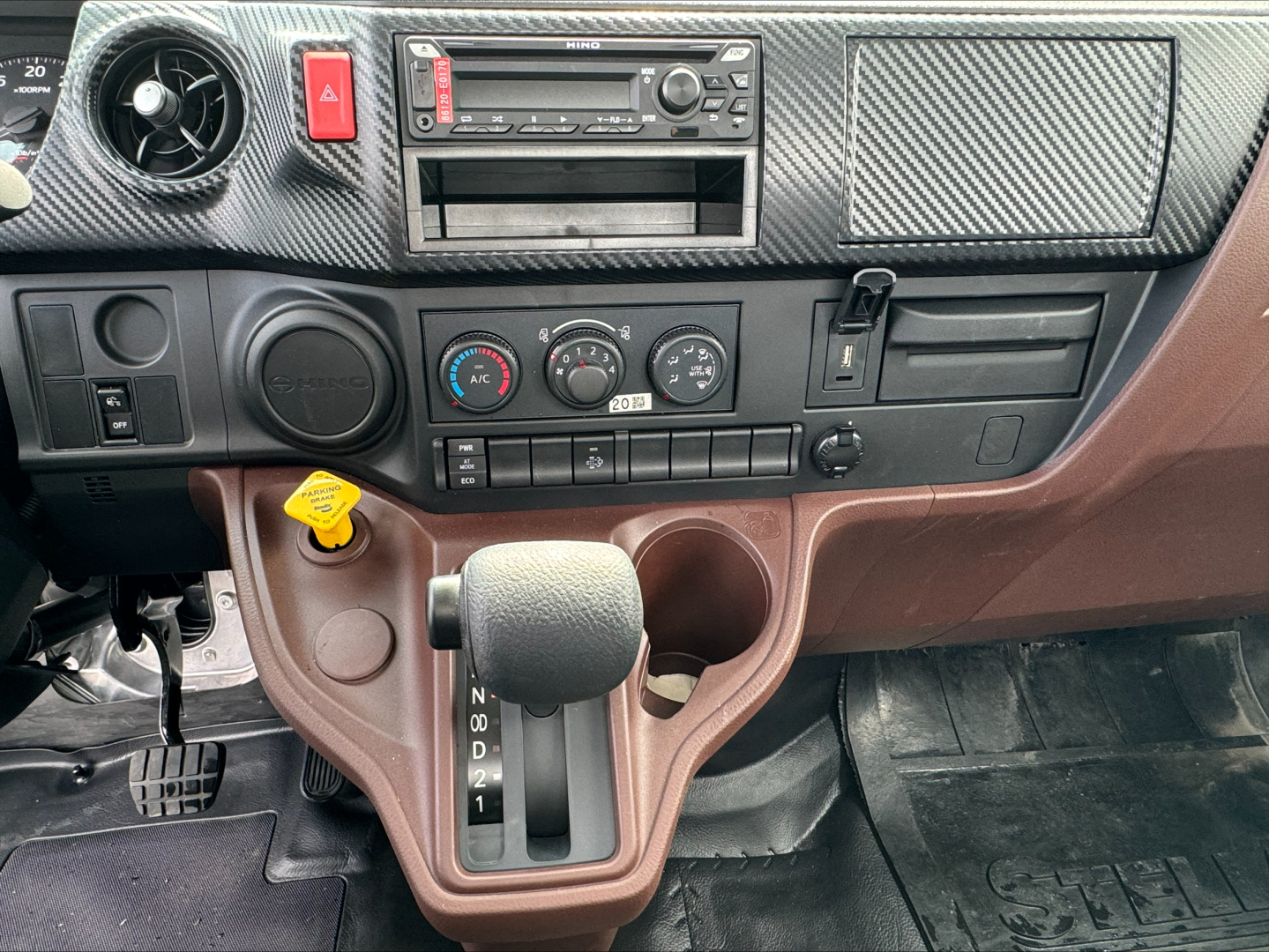 Dashboard of a cab and chassis truck with steering column and gear selector visible; includes climate control knobs, radio, hazard button, 4WD switch, cup holder, ignition area, and brown interior trim.