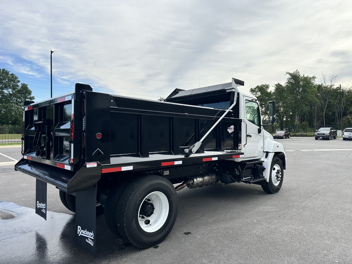 Truck cab and chassis with black dump bed in-service showing rear dump bed and hydraulic components, white cab, side mirrors, and stock number visible.