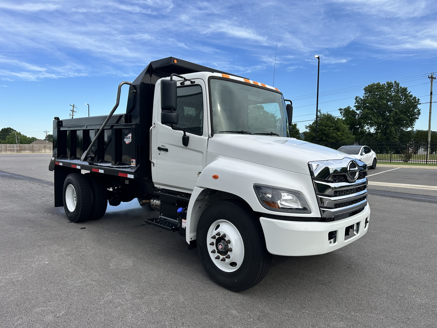Truck cab and chassis with white cargo bed, Hino logo on grille, black dump bed, front view showing clear headlights, side mirrors, and orange clearance lights