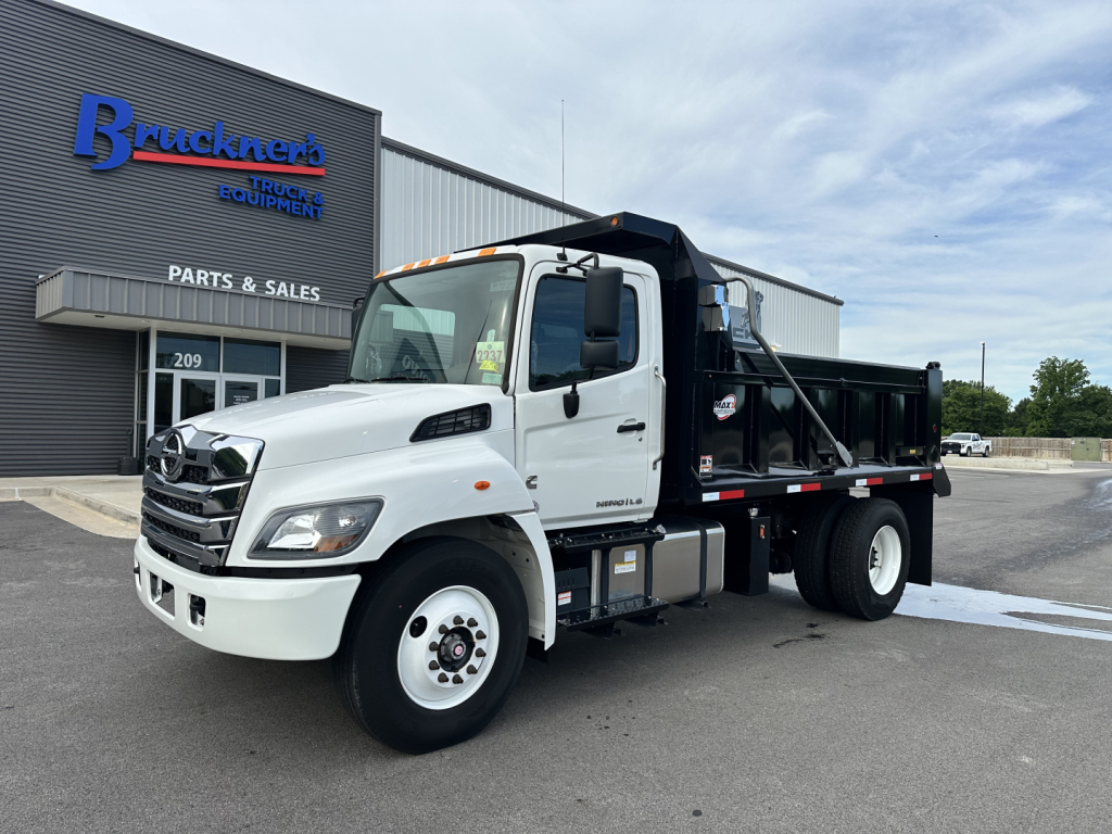 White 2025 Hino L7 dump truck in front of Brackner's equipment building with stock number 66566 and VIN 5PVNV7AJXS5T50068 visible on listing signage.