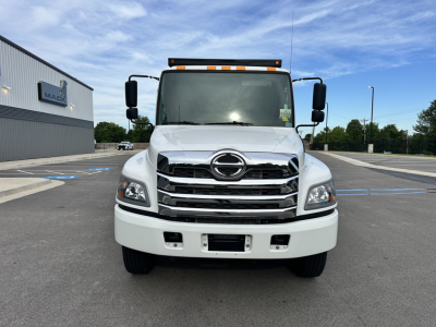Front view of a 2025 Hino L7 cab and chassis truck showing chrome grille, large headlights, and Hino emblem; clear windshield, side mirrors, and amber cab roof lights.