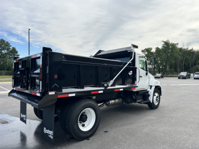 Truck cab and chassis with black dump bed in-service showing rear dump bed and hydraulic components, white cab, side mirrors, and stock number visible.