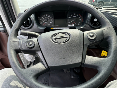 Cab and chassis dashboard view showing steering wheel with Hino logo and instrument cluster, left and right stalks, yellow tag visible