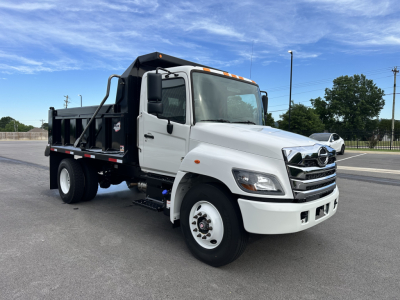 Truck cab and chassis with white cargo bed, Hino logo on grille, black dump bed, front view showing clear headlights, side mirrors, and orange clearance lights