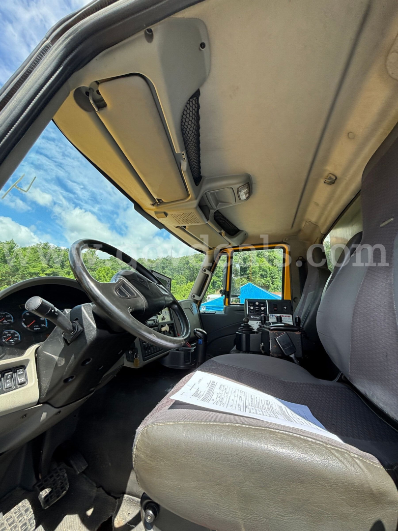 Truck cab interior of a 2013 International 7600 dump truck seen from the driver’s side door, with steering wheel, dashboard, and paperwork on the passenger seat.