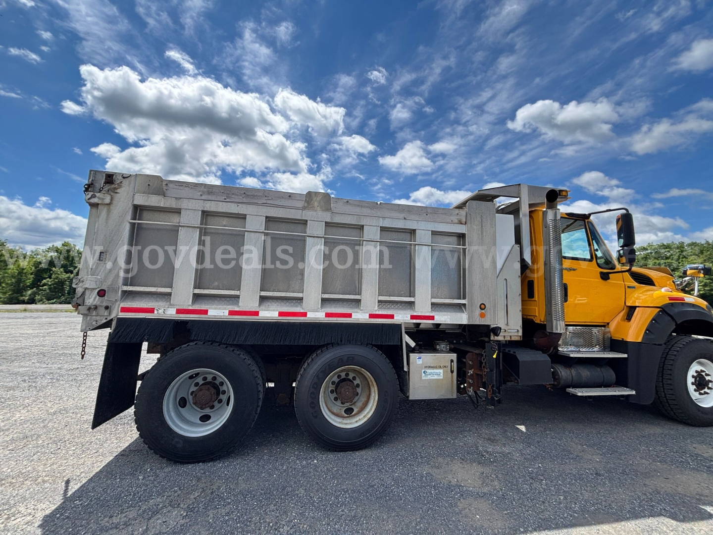 Dump truck side view showing dump bed and cab of International 7600 with yellow cab and gray bed.