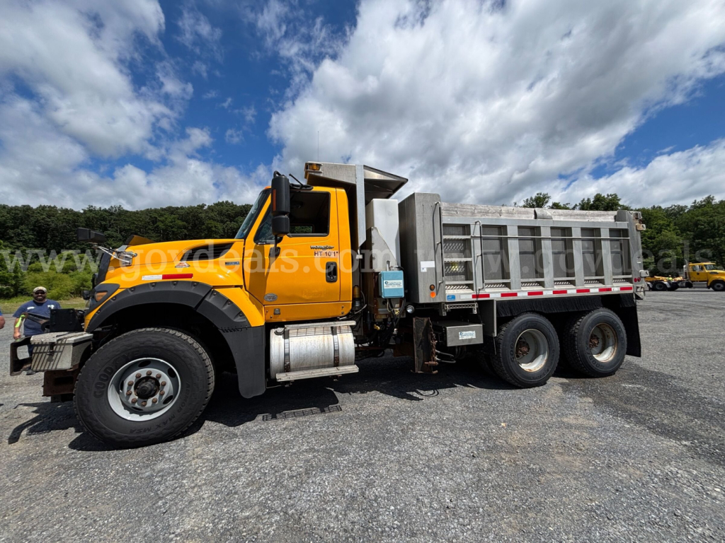 Dump truck side view showing bright orange International 7600 with silver dump bed and six wheels, stock number 30360 in background.