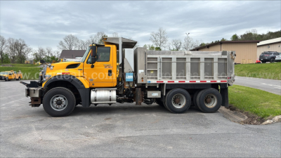 Dump truck showing bright yellow International cab and gray dump body in a parking lot.